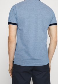 Polo à manches courtes bleu avec un tissu texturé, un col et des poignets de manches bleu marine contrastants, et des fentes latérales à l'ourlet.