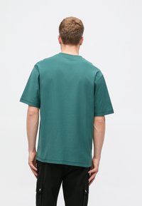 Tyrkysové bavlnené tričko s okrúhlym výstrihom a krátkymi rukávmi, s voľným strihom a minimálnym švom na leme.