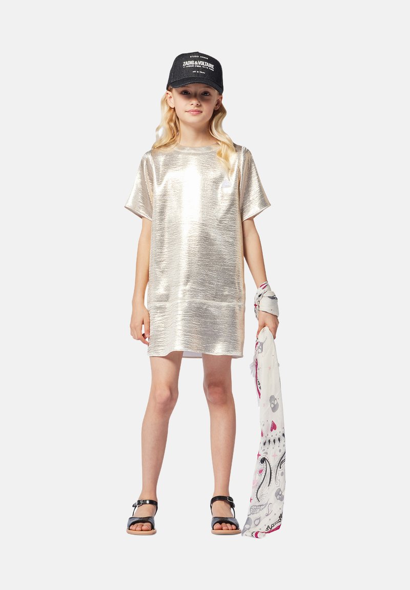 Metallic silver short-sleeve dress with a relaxed fit, paired with a black cap and patterned scarf; girl wearing black sandals.