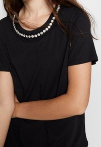 Svart t-shirt med rund halsringning prydd med blommig pärldekoration. Korta ärmar, mjukt tyg med avslappnad passform.