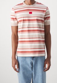 Stripet bomulds t-shirt med horisontale linjer i nuancer af koral, creme og beige, med et rødt firkantet logo på brystet.