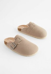 Beiga tofflor i mjukt mocka med spänne, med en tan korkfotbädd och en texturerad gummisula.