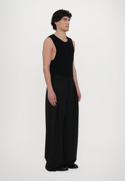 Black sleeveless tank top with a fitted design paired with oversized black trousers featuring a high waist and pleated front. Smooth texture.