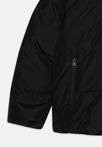 Manica di un giubbotto nero imbottito con design trapuntato, dotata di tasca laterale con zip. Il materiale appare liscio e resistente all'acqua.