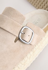Sandalo beige in camoscio senza lacci con fibbia quadrata in argento e suola intrecciata in juta. Caratterizzato da una texture morbida e un design semplice con cinturino.