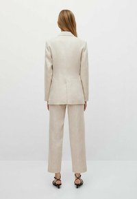 Beige-puuvilla-puku, jossa on muotoutunut bleiseri ja suorat housut. Sujuva pinta, jossa on hienoa kiiltoa, ja minimaalista ompeluainetta.