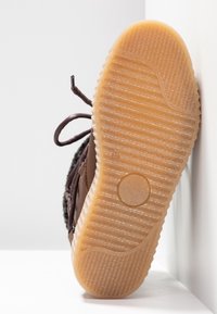 Zapato marrón con una suela de goma texturizada, que presenta un agarre con patrón y un borde redondeado. Los cordones oscuros se entrelazan a través de ojetes de metal.