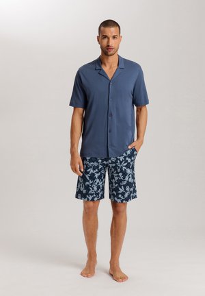 Chemise à manches courtes avec boutons en bleu foncé, associée à un short floral à motifs marins. Tissu léger, coupe décontractée et texture douce.