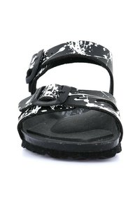 Sandal con motivo a macchie in bianco e nero, dotato di due cinturini regolabili, suola piatta e suola texturizzata scura. Design e costruzione minimalista.