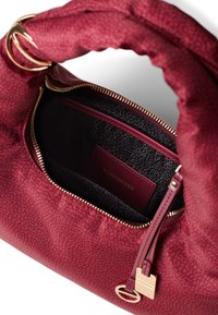 Burgundy handbag featuring a textured exterior, gold hardware, and a zip closure. Interior lined with dark fabric and branded tag visible.