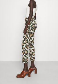 Pantalons à motif camouflage dans des tons de vert et beige, fabriqués en matériau léger ; associés à des sabots à talons marron.