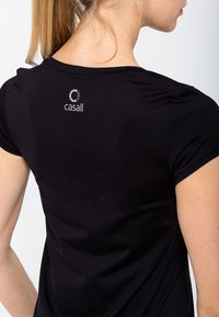 Camisa negra de manga corta hecha de tejido suave. Presenta un pequeño logo blanco en la parte posterior, cerca del escote.