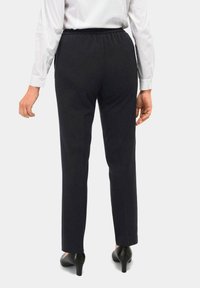 Zwarte broek met elastische tailleband en rechte pijpen. Gedragen met een witte blouse met lange mouwen en zwarte hoge hakken.