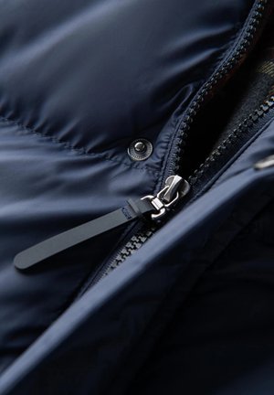 Chaqueta tipo puffer azul marina con cremallera metálica, cierre con botones a presión y acentos de tela. Textura suave con un patrón acolchado en la superficie.