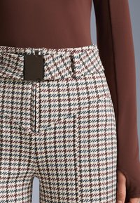 Trendy vzorované nohavice s dizajnom houndstooth v bielej, námorníckej a burgundskej farbe, doplnené pevným hnedým opaskom a hladkou textúrou.