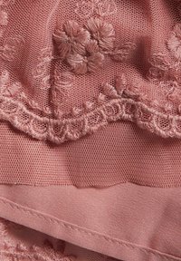 Tissu en dentelle délicate rose pâle présentant des motifs floraux brodés et une bordure festonnée, superposé sur une base en satin lisse.