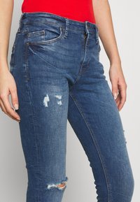 Jeans de mezclilla en azul medio con detalles desgastados, que cuentan con un corte slim, cierre de cremallera y bolsillos. Tejido texturizado con un ligero estiramiento.