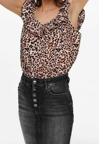Top bez rukávů s leopardím potiskem a volánkovým výstřihem, který je kombinován s černou džínovou sukní s vysokým pasem a pěti předními knoflíky.