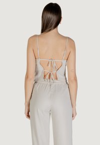 Blusa grigia chiara senza schiena con sottili spalline e dettaglio a fiocco sul retro, realizzata in un tessuto morbido e liscio. Abbinata a pantaloni coordinati.