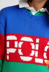 Garnslagen tröja med djärva blå, röda och gröna ränder, med stora vita "POLO"-bokstäver i mitten och ribbad halsringning.