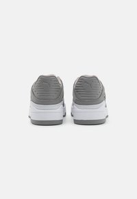 Scarpe da ginnastica grigie e bianche con un retro grigio testurizzato, colletto imbottito e intersuola bianca. Presenta dettagli del logo sul tallone.