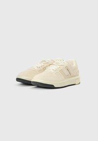 Beežid seemisnahast tossud, millel on augustatud pealiskate, lamedad paelad ja kontrastne must kummist tallaga. Omavad nurgelist disaini ja brändielementi.