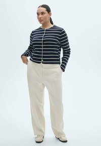 Mornarsko plava i bijela prugasta kardigan dugih rukava s zlatnim gumbima, uparen s krem hlačama širokih nogavica i svijetlim loafericama.