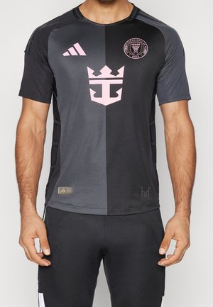 Homme portant un maillot de football noir et gris foncé avec un logo Adidas rose, un écusson du Club Internacional de Futbol Miami, et un emblème de couronne rose.