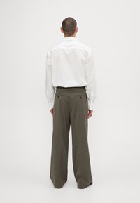 Vit långärmad skjorta med spetsig krage, kombinerad med vida, olivgröna byxor, båda med en mjuk textur och bakfickor.