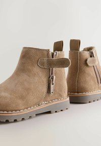 Bottines en daim marron avec fermeture éclair et sangle élastique. Tige texturée, bout rond et semelle en caoutchouc avec motif de traction. Design léger.