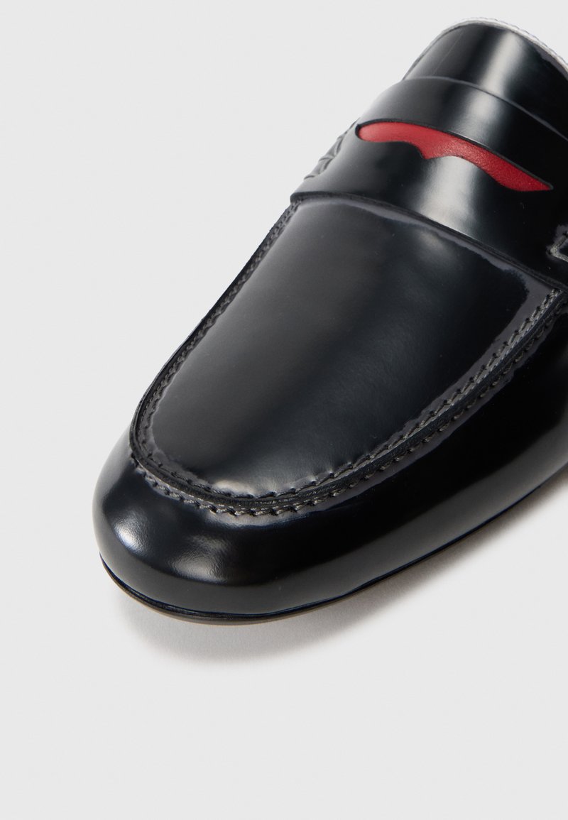 Sort læder loafers med en glat overflade, et syet design og en fremtrædende rød detalje på vampen for ekstra flair. Rundt tåform.