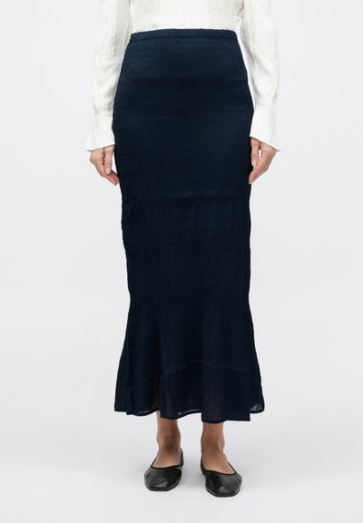 Tumesinine kihiline maksiseelik tekstuurse kangaga, millel on liibuv vöökoht. Kandmisega mustad tasased kingad ja pikad varrukadhele hele särk.