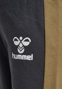 Grå och tanfärgade sweatpants med en mjuk textur. Har en vit Hummel-logotyp och en unik design inspirerad av bin på vänster ben.