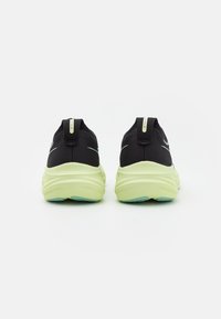 Zapatillas deportivas negras con parte superior de malla transpirable, con una suela y talón de color verde lima, un asa y acentos reflectantes mínimos.