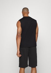 Maglietta nera senza maniche realizzata in tessuto morbido, con colletto rotondo e vestibilità comoda. Accompagnata da pantaloni corti neri, che mostrano un design semplice e minimale.