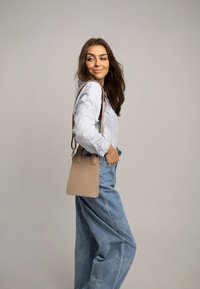 Beżowa skórzana torba o uporządkowanym kształcie, prostokątnym designie i dwóch górnych uchwytach. Zestawiona z jasnoniebieską koszulą i dżinsami w gwiazdy.