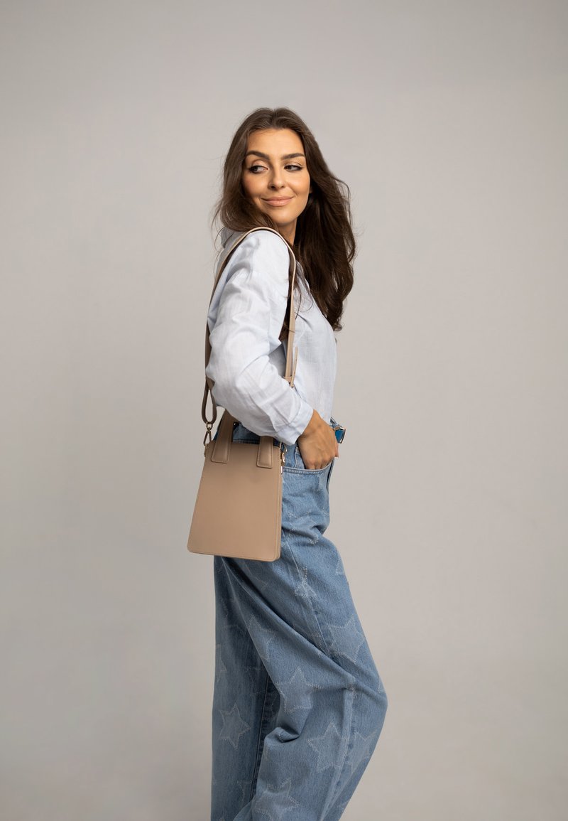 Beżowa skórzana torba o uporządkowanym kształcie, prostokątnym designie i dwóch górnych uchwytach. Zestawiona z jasnoniebieską koszulą i dżinsami w gwiazdy.