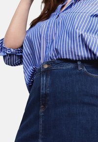Camisa de botones a rayas azul y blanca con mangas enrolladas, combinada con una falda de mezclilla oscura con cierre de botones en la parte delantera y bolsillos.