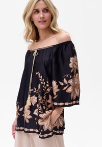 Bluzka na ramiączkach w czarnym materiale z złotymi haftami kwiatowymi. Posiada pleciony sznurek przy dekolcie i luźne, szerokie rękawy.