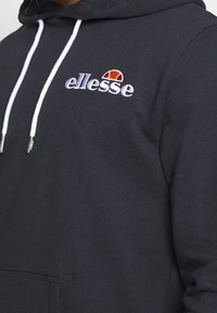 Czarna bluza z kapturem wykonana z bawełnianej mieszanki materiałów z białymi sznurkami. Posiada haftowane logo "ellesse" oraz kolorowy akcent nad logo.
