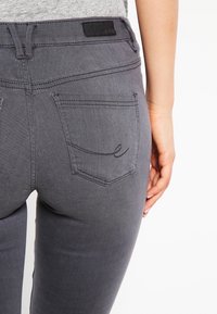 Gray denim jeans with a slim fit. Features a back pocket with a stitched "e" logo and standard stitching details.