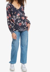 Blusa floreale navy con scollatura a V, maniche a palloncino e dettaglio con fiocco. Abbinata a jeans dritti blu chiaro e sneakers bianche.