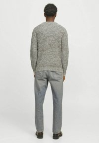 Suéter de punto gris con un patrón texturizado, escote redondo y mangas largas, combinado con jeans rectos de color gris claro y zapatos negros.