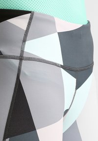 Leginsy w geometryczny wzór w odcieniach szarości, miętowym i jasnoróżowym. Gładki, elastyczny materiał z płaskimi szwami dla wygody.