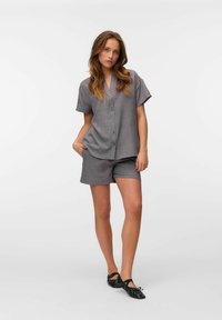 Camisa de manga corta a rayas grises con botones, combinada con pantalones cortos a juego. Zapatos planos negros con textura fruncida.
