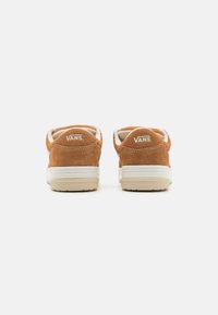 Brune suedé sneakers med hvite detaljer og en teksturert gummisåle. "VANS"-logo sydd på hælen. Rund tå og lav toppdesign.