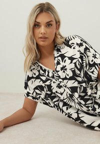 Svart och vit blommig blus med avslappnad passform, korta ärmar och v-ringning. Mjuk tyg med stora blom- och bladmönster.