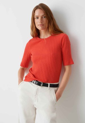 Top rosso a righe con maniche corte e scollo rotondo, abbinato a pantaloni bianchi a vita alta e una cintura nera. Tessuto morbido.