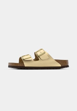Gold vegan leather sandals with two adjustable straps, cork footbed, and dark rubber sole. Smooth texture with metallic finish.