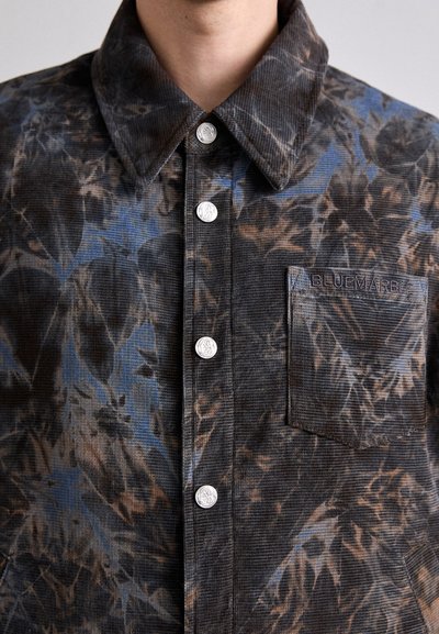 Corduroy shirt in dark brown with blue and rust floral pattern, featuring a pointed collar, silver snap buttons, and a chest pocket with logo.